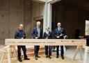 Vier festlich gekleidete Personen posieren vor einem symbolischen Holzbalken