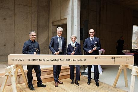 Vier festlich gekleidete Personen posieren vor einem symbolischen Holzbalken