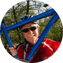 A man with sun glasses and a helmet holding a bike in front of him