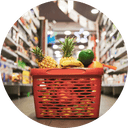 A shopping basket full of groceries stands in an aisle in a supermarket.