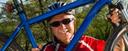Ein Mann mit Helm und Sonnenbrille hält ein blaues Fahrrad vor sich