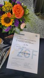 Urkunde für den 3. Platz bei einer Posterausstellung, daneben ein bunter Blumenstrauß