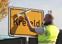 Ein Mann reinigt ein Ortseingangsschild von Krefeld.