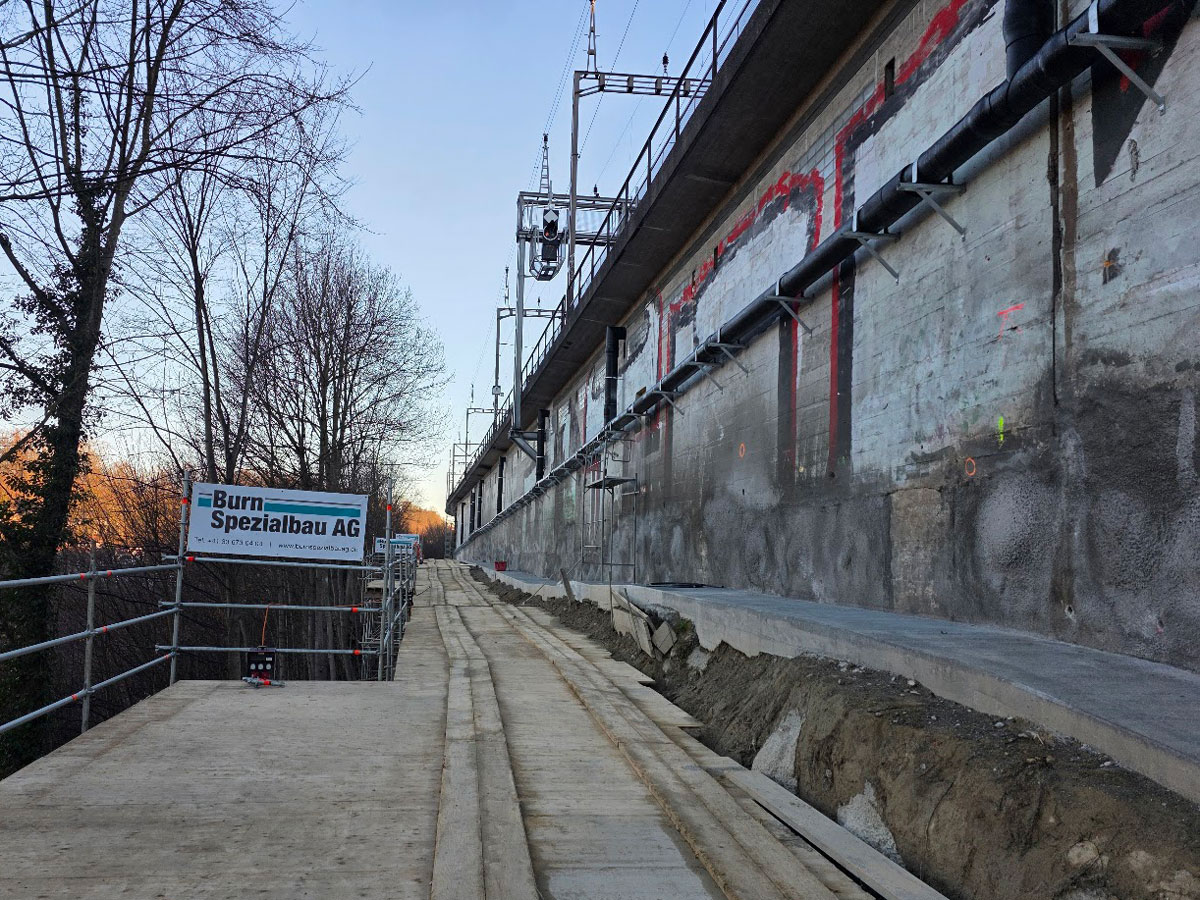 Baustelle der Burn Spezialbau AG entlang des Bahnviadukts mit Spritzbetonwand, Unterhaltsweg und Zugangsbereich.