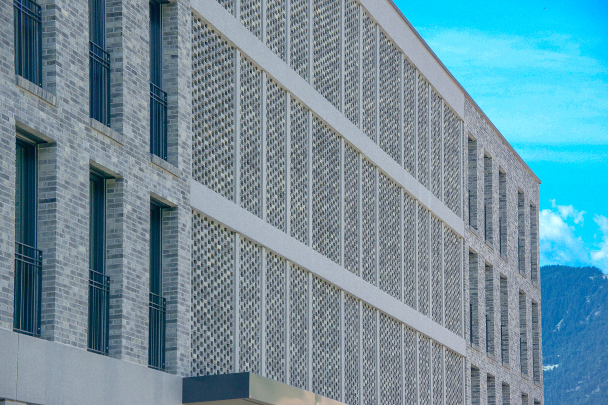 Hellgraue Sichtmauerwerk-Fassade der Staziun Domat-Ems mit durchlässig gemauerten Fassadenfeldern.
