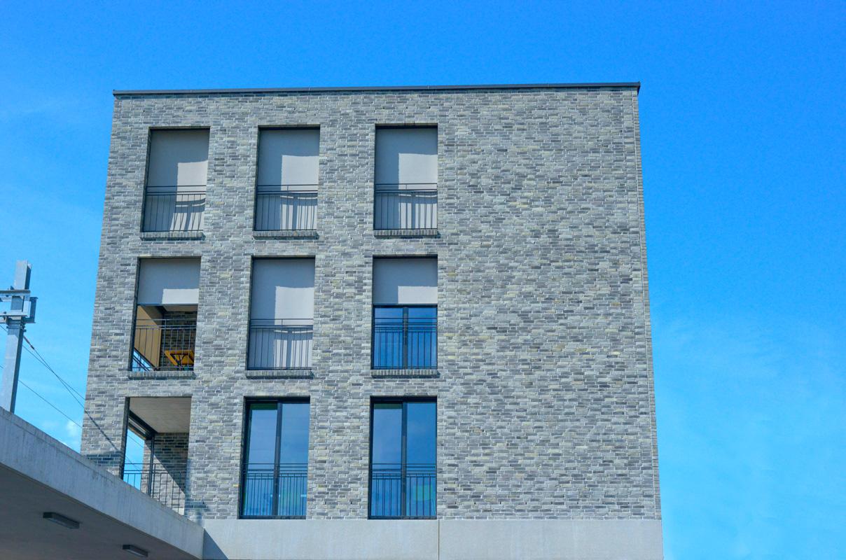Fassade des Bahnhofgebäudes in Domat-Ems mit hellgrauem Sichtmauerwerk.