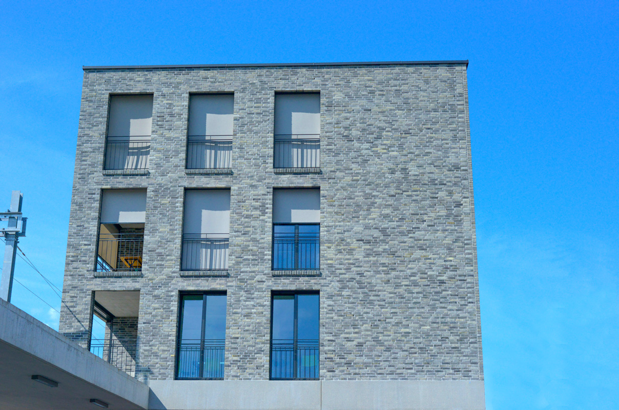 Fassade des Bahnhofgebäudes in Domat-Ems mit hellgrauem Sichtmauerwerk.