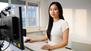 Eine Frau arbeitet an ihrem Computer und guckt in die Kamera