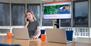 Junge Frau telefoniert in einem Büro, vor ihr stehen ein Laptop und eine orangefarbene Tasse.