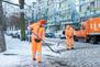 Zwei BSR-Mitarbeitende streuen mit Schaufeln eine verschneite und vereiste Straße. Im Hintergrund ist ein Fahrzeug der BSR zu erkennen.