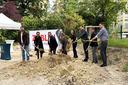 Mehrere Personen vor einem Erdhügel führen symbolischen Spatenstich durch