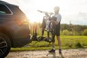 Ein Mann in Sportbekleidung steht hinter seinem PKW und hebt sein Fahrrad auf den Fahrradhalter für das Auto