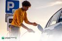 Junger Mann, der ein Ladekabel in sein E-Auto steckt, um es aufzuladen