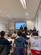 Zwei Mitarbeitende von Consors Finanz stehen lächelnd in einem Klassenraum vor einer Schulklasse und halten einen Workshop zum Thema Finanzbildung ab.