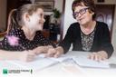 Oma sitzt am Tisch mit ihrer Enkelin und erklärt ihr etwas