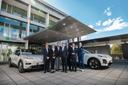 Im Vordergrund stehen insgesamt sechs Männer und eine Frau, sie lächeln und tragen alle Anzüge und stehen vor zwei Elektroautos. Im Hintergrund ist ein Bürogebäude mit Arval-Schriftzug und blauer Himmel zu erkennen.