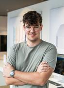 Ludwig Krayl, Head of eCommerce der compustore Group, trägt ein hellgraues T-Shirt und eine Brille. Er blickt mit verschränkten Armen lächelnd in die Kamera.