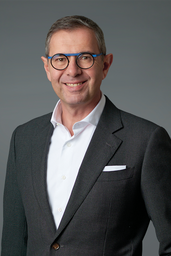 Michel Thebault, CEO von Consors Finanz, trägt einen dunklen Anzug, eine drunkle Brille und lächelt freundlich in die Kamera.