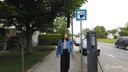 Astrid Drechsel-Grau geht an der Ladesäule vorbei und weg von ihrem Fahrzeug. Rechts von ihr ist ein Hinweisschild für vorhandene Ladesäulen.