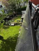 Ein Balkonkraftwerk ist an einem Balkon eines Hauses befestigt. Im Hintergrund ist ein Garten mit grünem Rasen.