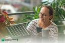 Frau mit Kaffeetasse auf ihrem Balkon blickt freundlich auf ein Solarpanel, das vor ihr liegt.