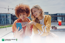 Eine Frau zeigt einer anderen einen Tipp auf ihrem Smartphone zu einem typischen Handy Ladefehler.