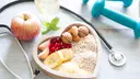 Healthy food in a heart-shaped bowl, with a glass of water, an apple and dumbbells around it