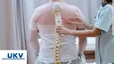 nurse holding spine model against the patients backs with clientlogo UKV