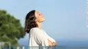 Adult woman breathing fresh air in a balcony in front of the ocean