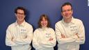 Adrian Thiessen, Joana Hauff und Benjamin Hebborn stehen nebeneinader mit verschränkten Armen vor einer blauen Wand. Sietragen weiße Pullover mit Thieme und Relias Logo.