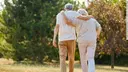 Two older peolple are walking in the nature, you see them from behind and the have their arms around eachother