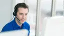 Man calling someone with a headset and sitting in front of his computer