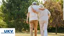 Two older peolple are walking in the nature, you see them from behind and the have their arms around eachother with clientlogo UKV