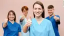 Vier Pflegende in Arbeitskleidung schauen in die Kamera. Sie strecken die Daumen hoch.