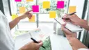 Two people work out a strategy, one person holds data in their hand and the other a pad for notes.