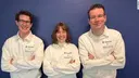 Adrian Thiessen, Joana Hauff und Benjamin Hebborn stehen nebeneinader mit verschränkten Armen vor einer blauen Wand. Sietragen weiße Pullover mit Thieme und Relias Logo.