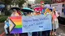Group of people standing in the rain at a parade, holding a banner with rainbow colors and the text “Thieme loves diversity – Because everyone counts!”.