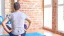 Middle age sportman sitting on mat at a gym. Sitting backwards, looking away with arms on body