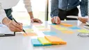 Two men are standing at a table with colored Post-Its stuck to it