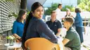 Several people sitting and standing on a terrace, having a conversation in a relaxed setting during daylight.