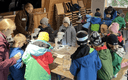 Maus-Türöffner-Tag 2024: viele Kinder stehen rund um einen Tisch und experimentieren mit etwas