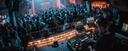 A DJ performs in a packed club, surrounded by dancing people