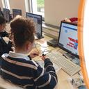 Eine junge Frau sitzt an einem Computer und wird von hinten fotografiert, wie sie experimentiert
