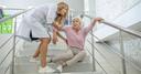 Seniorin, die auf der Treppe gefallen ist und der von einer jüngeren Krankenschwester aufgeholfen wird.