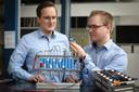 Two men examine parts of a battery.