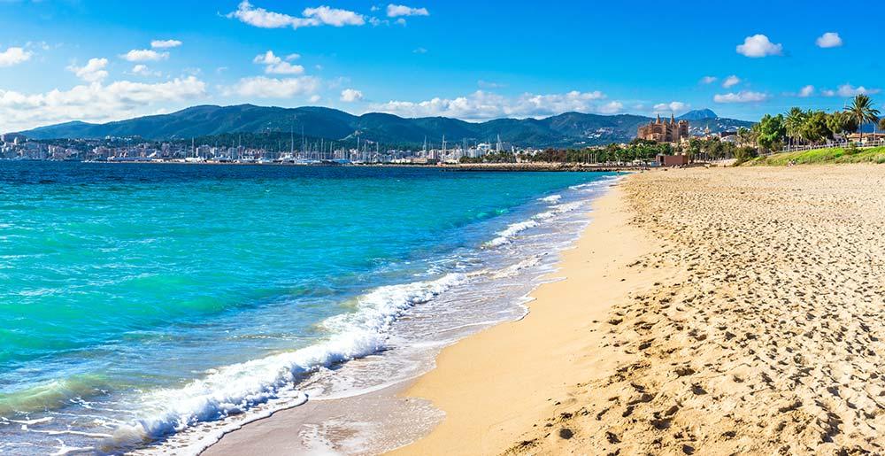 Blick auf den Strand in Palma de Mallorca mit Stadt und Hafen im Hintergrund