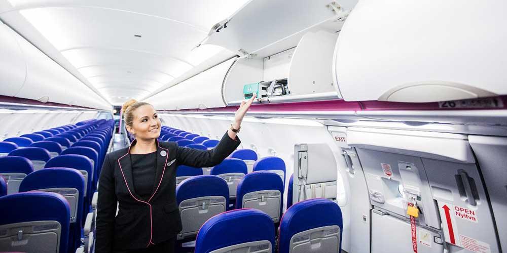 Flugbeleiterin an Bord eines Wizz Air-Flugzeugs zeigt das Fach für das Handgepäck.