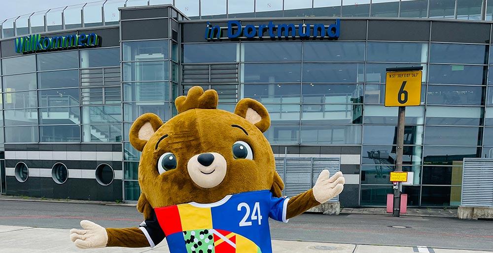 Das EM-Maskottchen steht auf dem Vorfeld des Dortmund Airport vor dem Schriftzug "Willkommen in Dortmund"