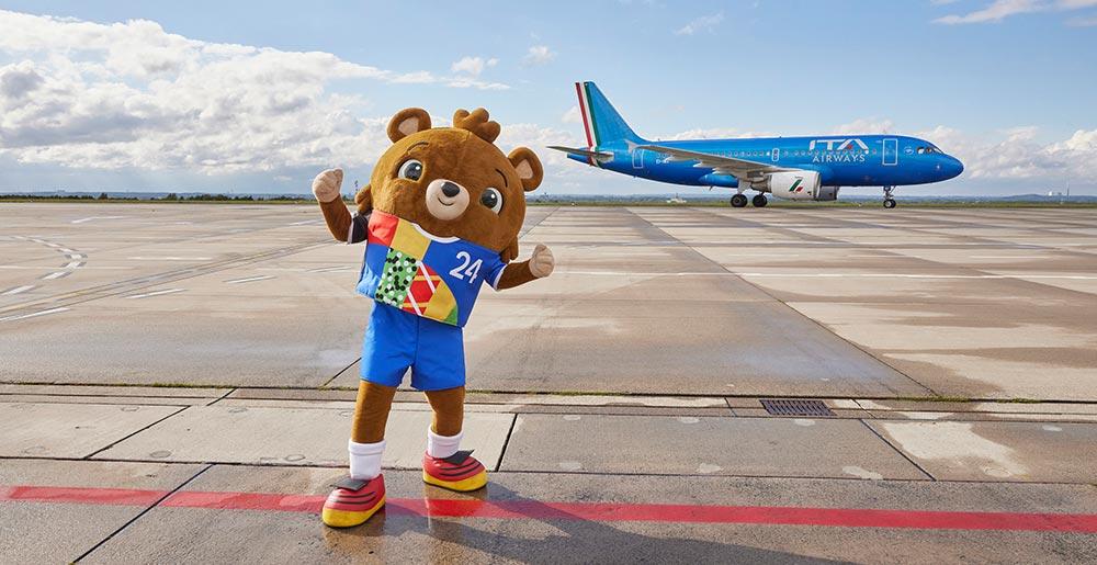 EM-Maskottchen vor einer Maschine der ITA Airways mit dem Italienischen Nationalteam an Bord auf dem Vorfeld des Dortmund Airport