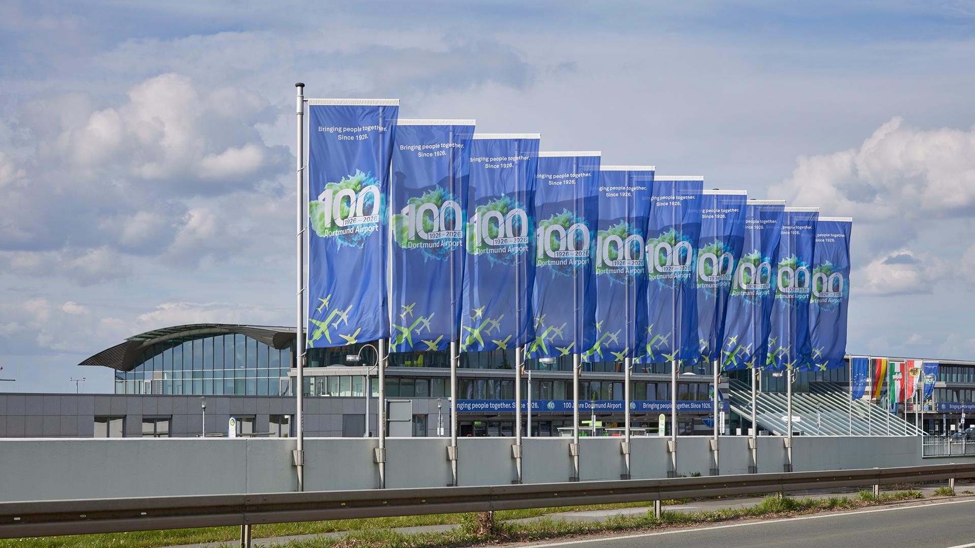 Flaggen mit dem 100-Jahre Logo vor dem Terminal des Dortmund Airport